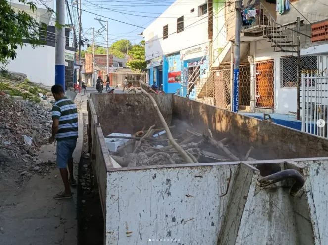 Contenedor grande de recolección de residuos ubicado en una calle del sector San Vicente de Paul, con ramas y objetos en su interior durante una jornada comunitaria.