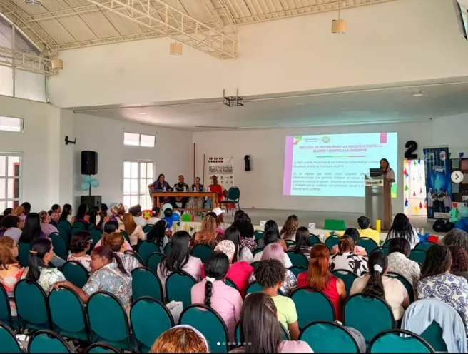 Ponente hablando desde un atril frente a una pantalla de proyección en un auditorio lleno de docentes y personal administrativo sentados en sillas.
