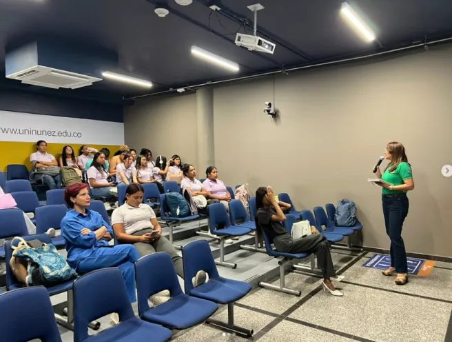 Ponente hablando con un micrófono ante un auditorio universitario con estudiantes sentados en sillas azules durante el conversatorio sobre identidades trans.