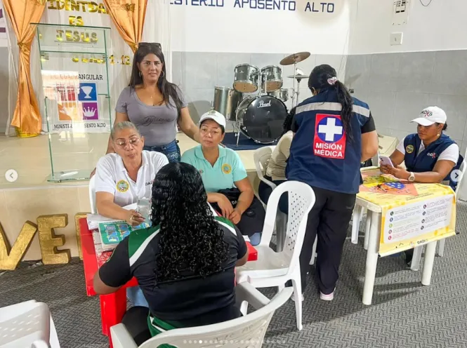Personal institucional atendiendo a los habitantes en mesas de registro y salud durante una jornada comunitaria en un espacio cubierto.
