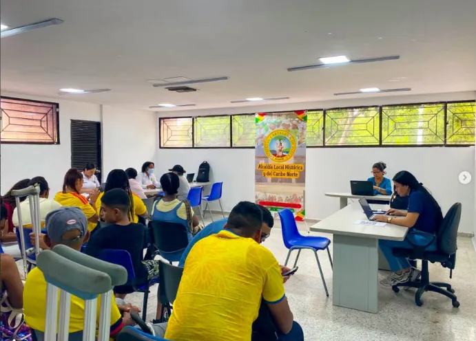 Ciudadanos siendo atendidos en escritorios por personal institucional durante una jornada de inscripción para la tarifa diferencial en un salón iluminado.