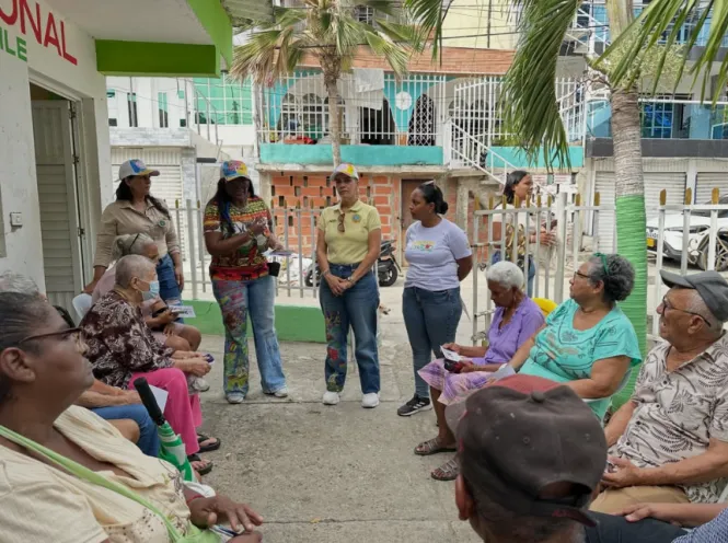 Un grupo de personas mayores se encuentra sentado al aire libre prestando atención a varias mujeres que conversan con ellos durante la jornada de atención comunitaria.