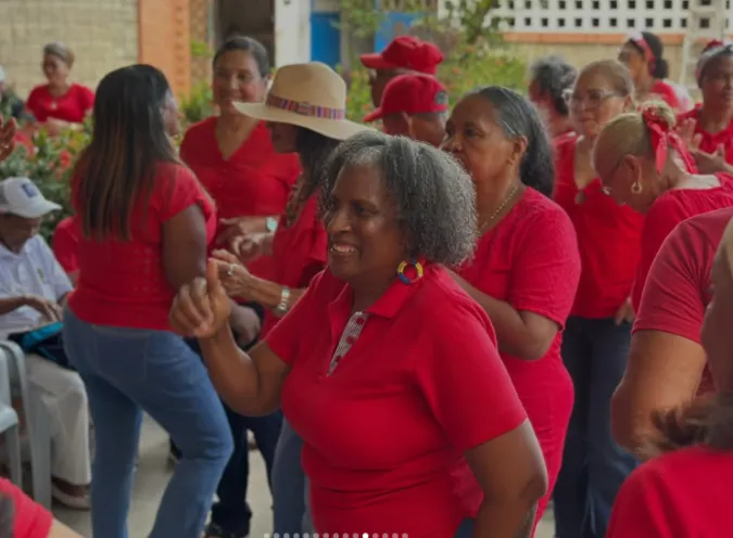 En la imagen se ve a un grupo de personas adultas mayores vestidas con prendas rojas celebrando con entusiasmo y sonrisas, con una mujer al frente haciendo una seña positiva con el pulgar.