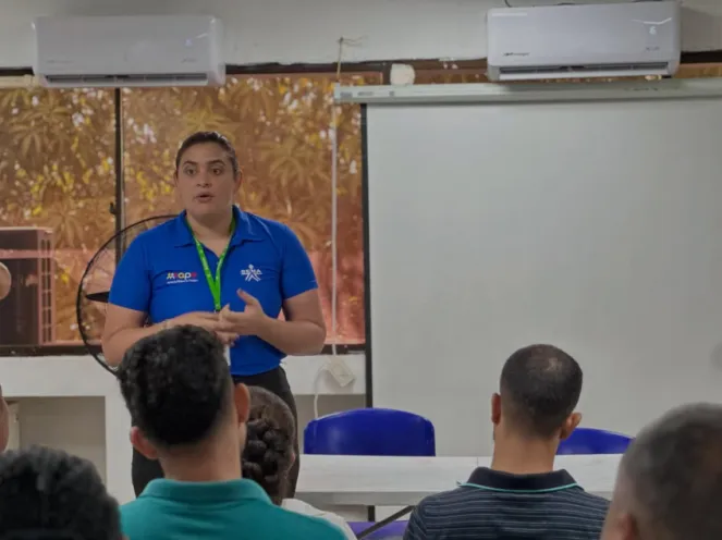 En la imagen se observa a una instructora impartiendo una charla informativa a un grupo de asistentes sentados en un salón, como parte de las actividades de orientación laboral.