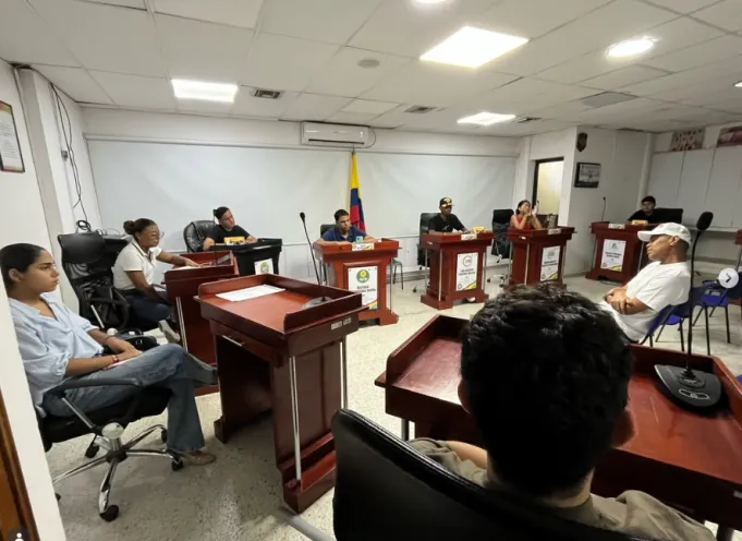 Fotografía en un recinto de reuniones institucional donde varias personas se encuentran sentadas en escritorios de madera durante una sesión de trabajo con el alcalde local.